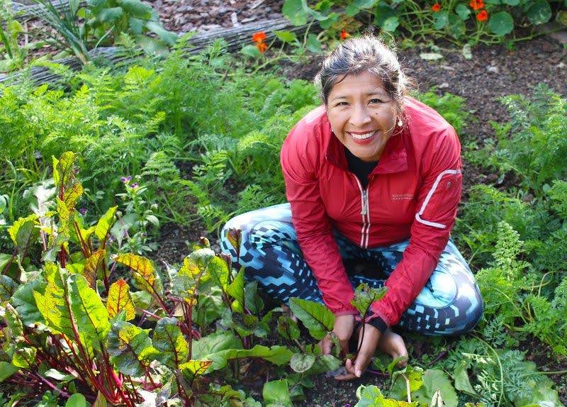 Mariaelena Huambachano sitting in a garden with a red overcoat and blue and white pattern leggings